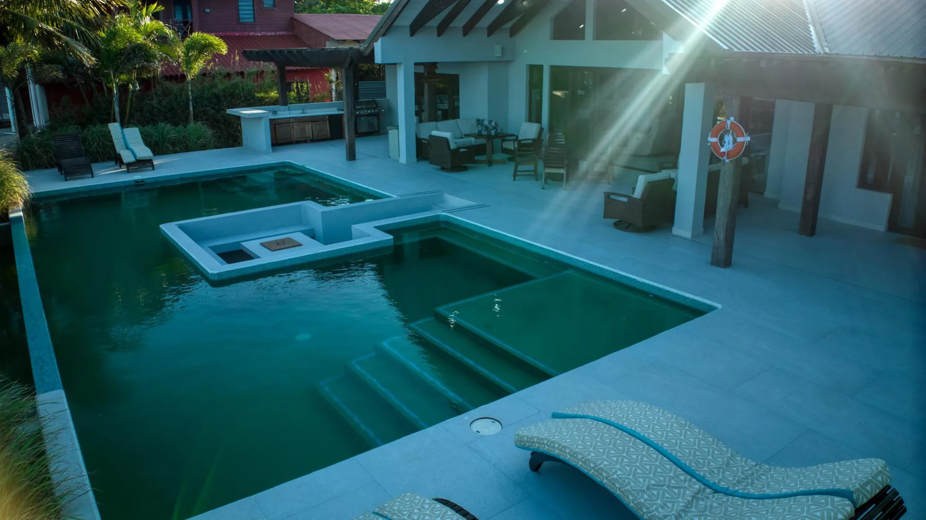 An outdoor swimming pool with submerged steps and lounge seating beside it.