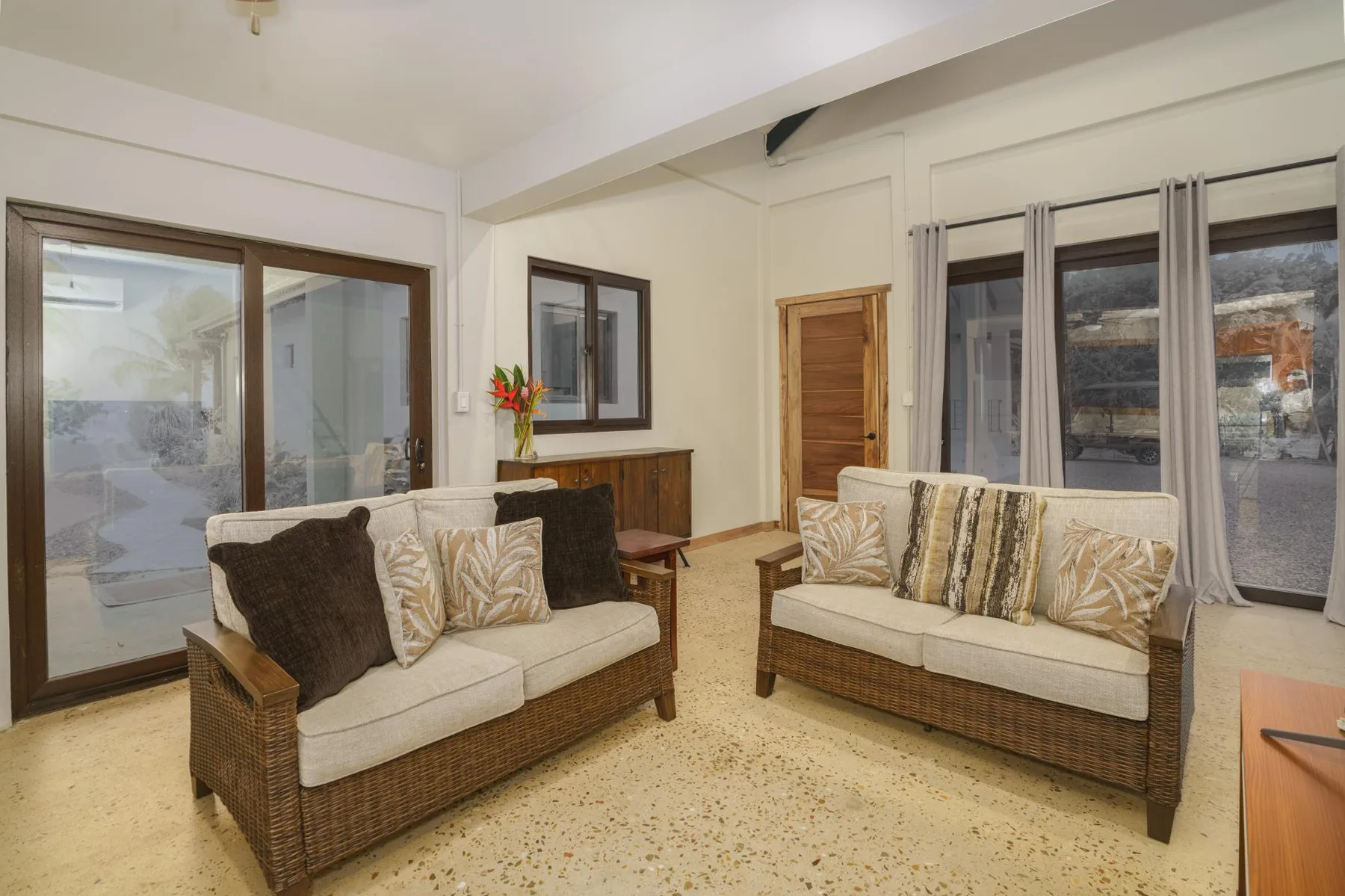 A living room with two wicker seating areas, neutral cushions, and large windows.