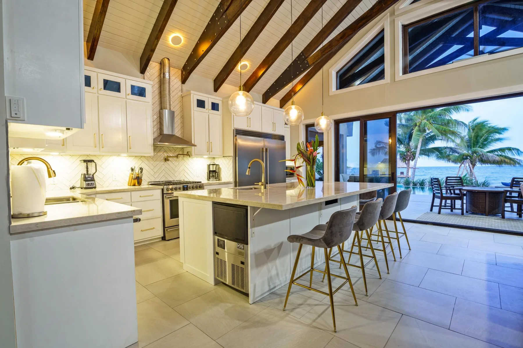 A bright kitchen with a central island and stools opens onto an outdoor patio.