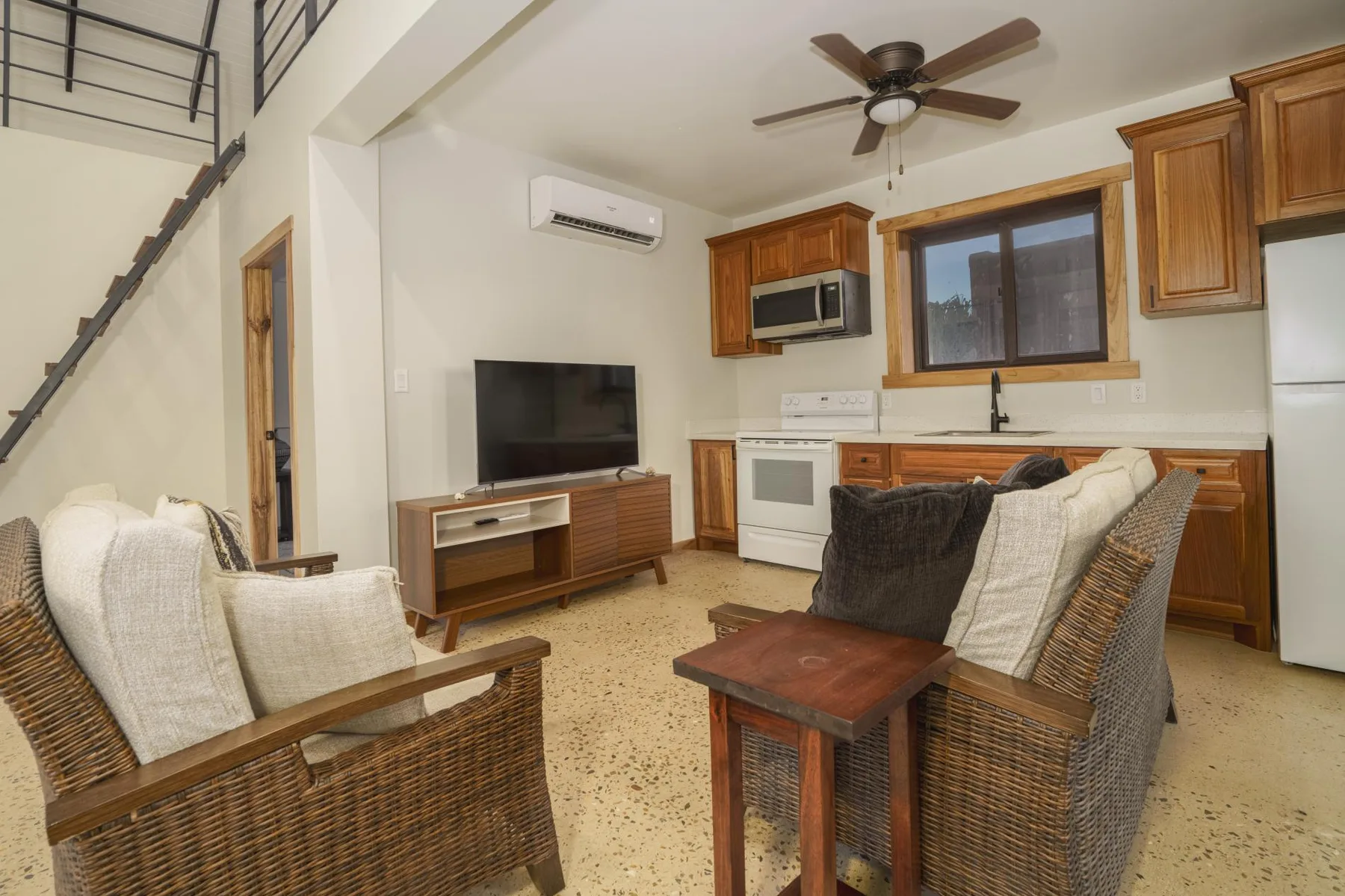 A living room with wicker seating, a television, and a kitchen area.