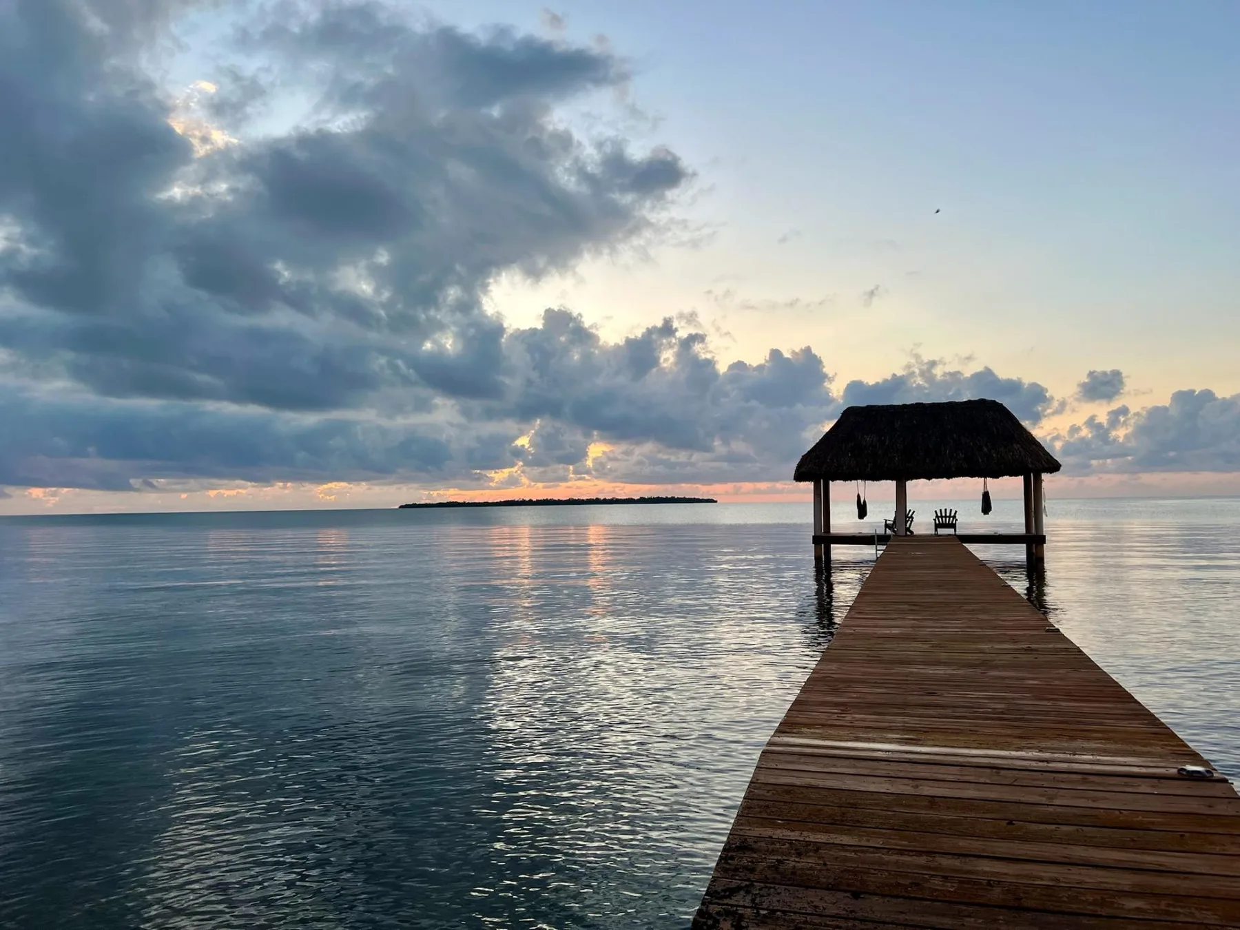 A wooden pier extends over calm water toward a thatched shelter at sunset.