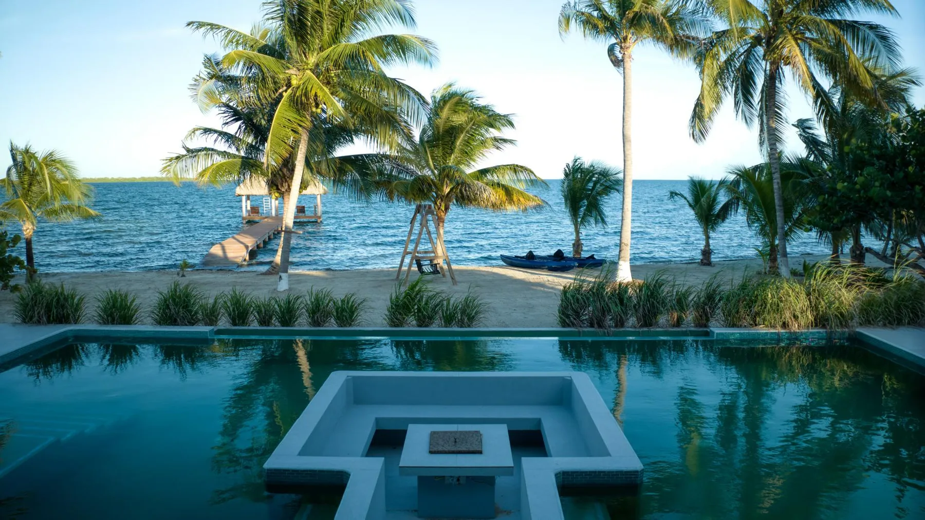 A swimming pool overlooks palm trees and the ocean.