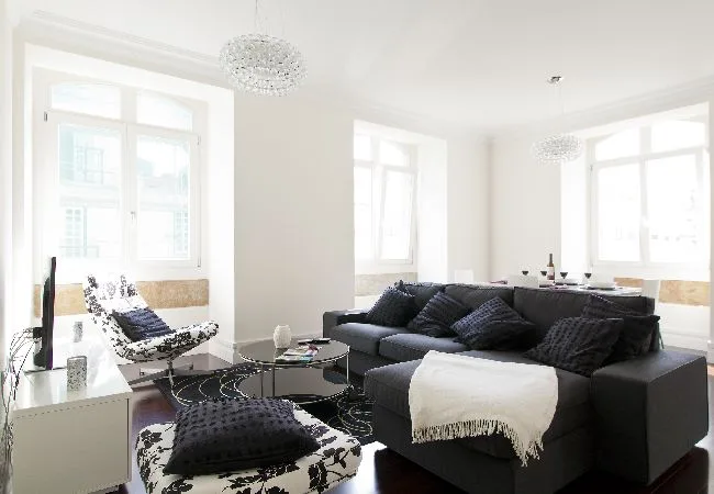 A bright living room with a dark sectional sofa and large windows.