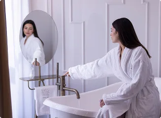 Espacio representativo del hotel: Un lavabo de baño con una mujer en bata frente a un espejo.