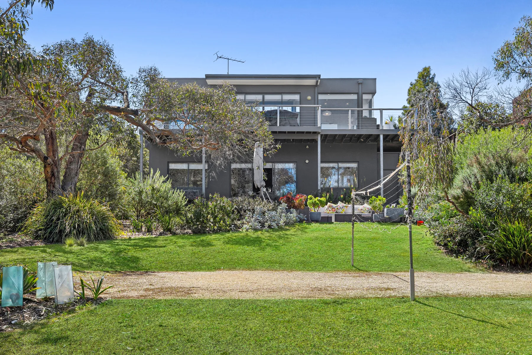 A modern house stands behind a green lawn and landscaped garden.