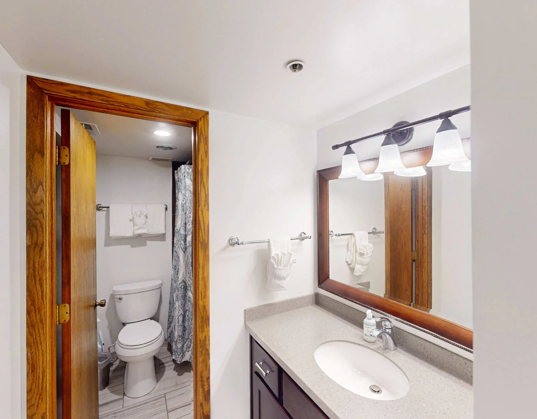 Vanidad de baño con lavabo y espejo junto a un espacio de inodoro abierto.