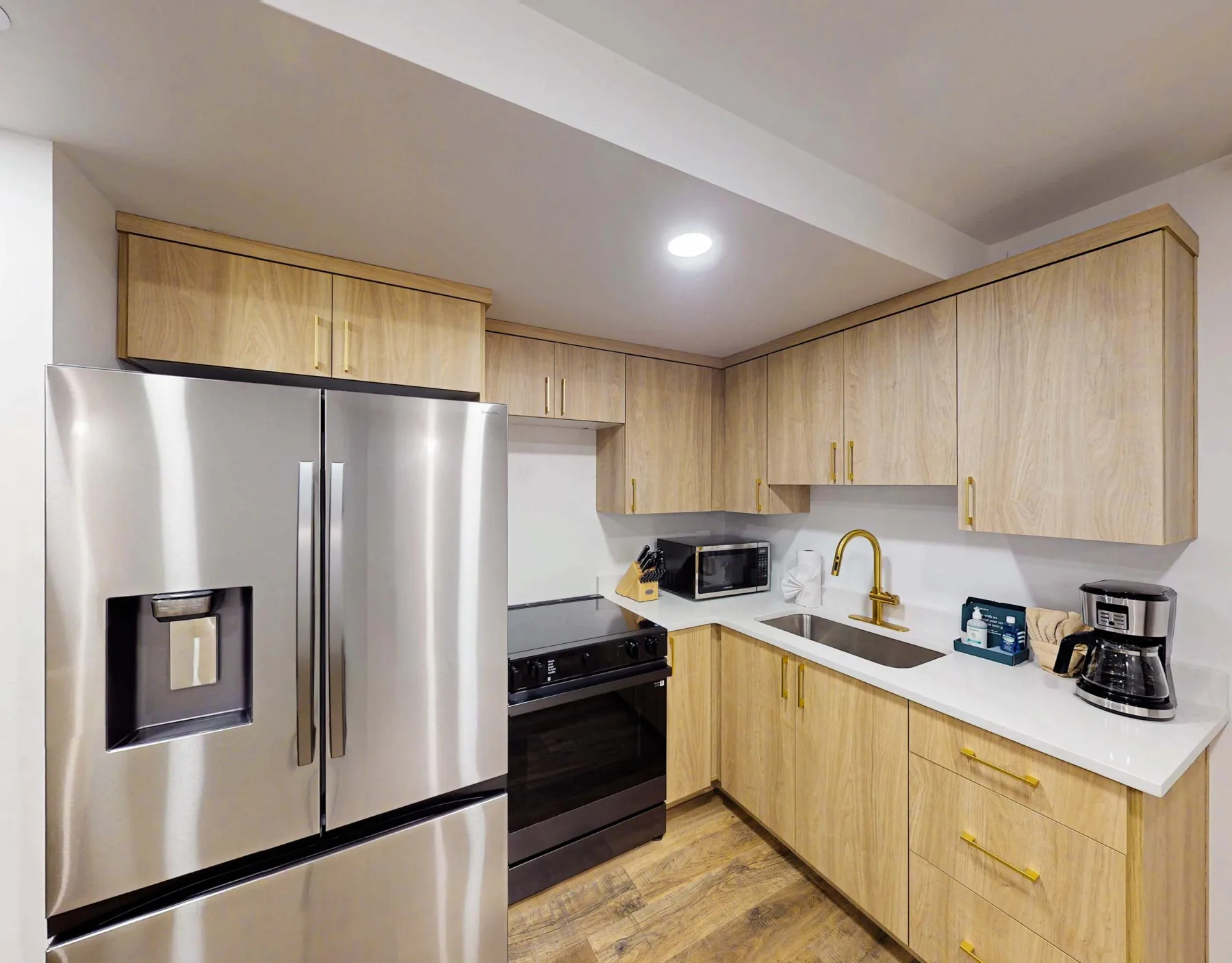 Una cocina moderna con gabinetes de madera clara, electrodomésticos de acero inoxidable y una encimera blanca.