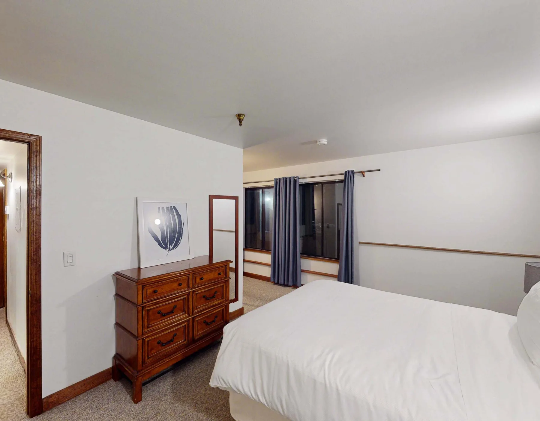 Un dormitorio con una cama blanca, una cómoda de madera y una ventana con cortinas.