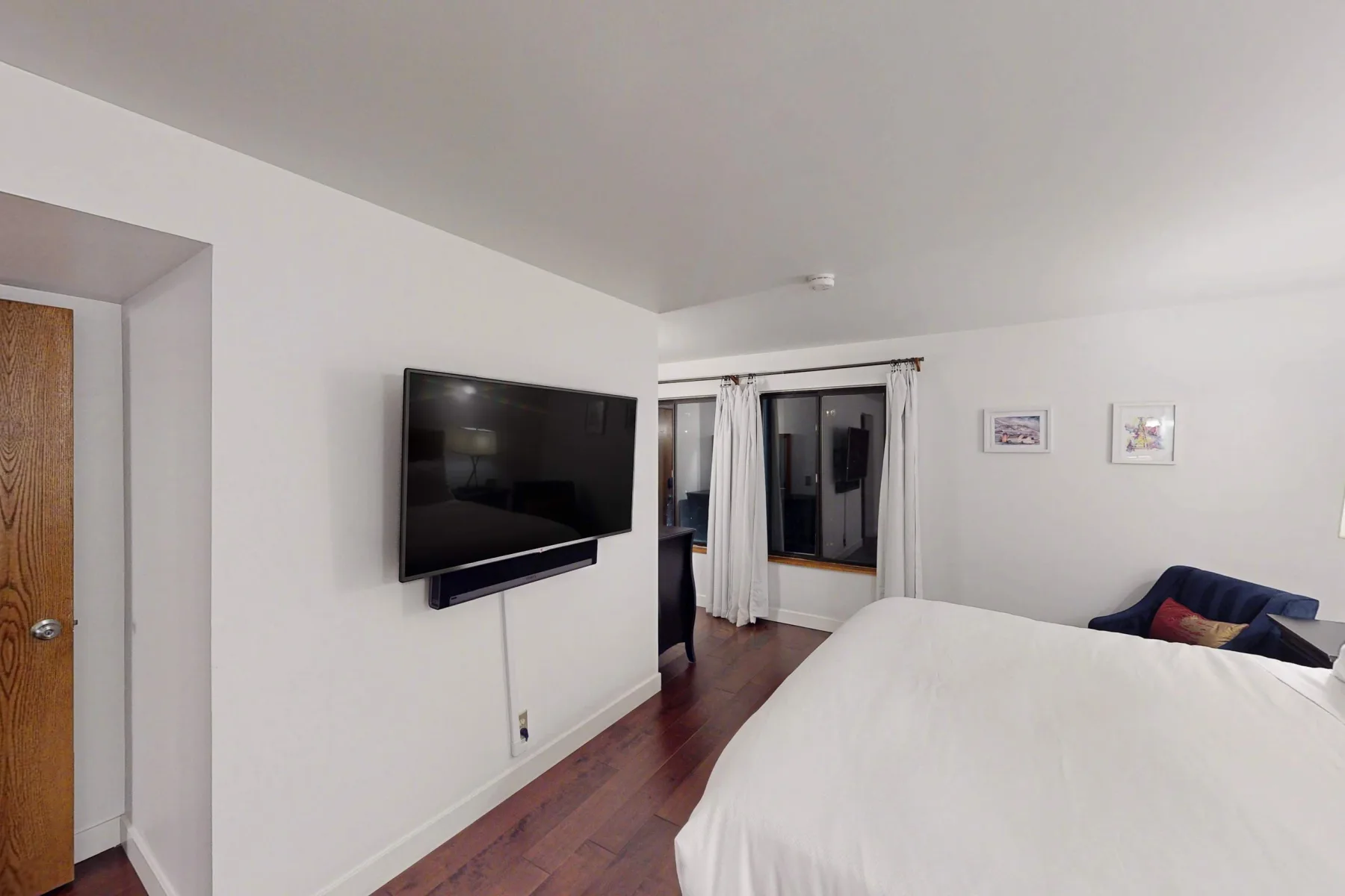 Un dormitorio con un televisor en la pared junto a una cama y una ventana con cortinas.