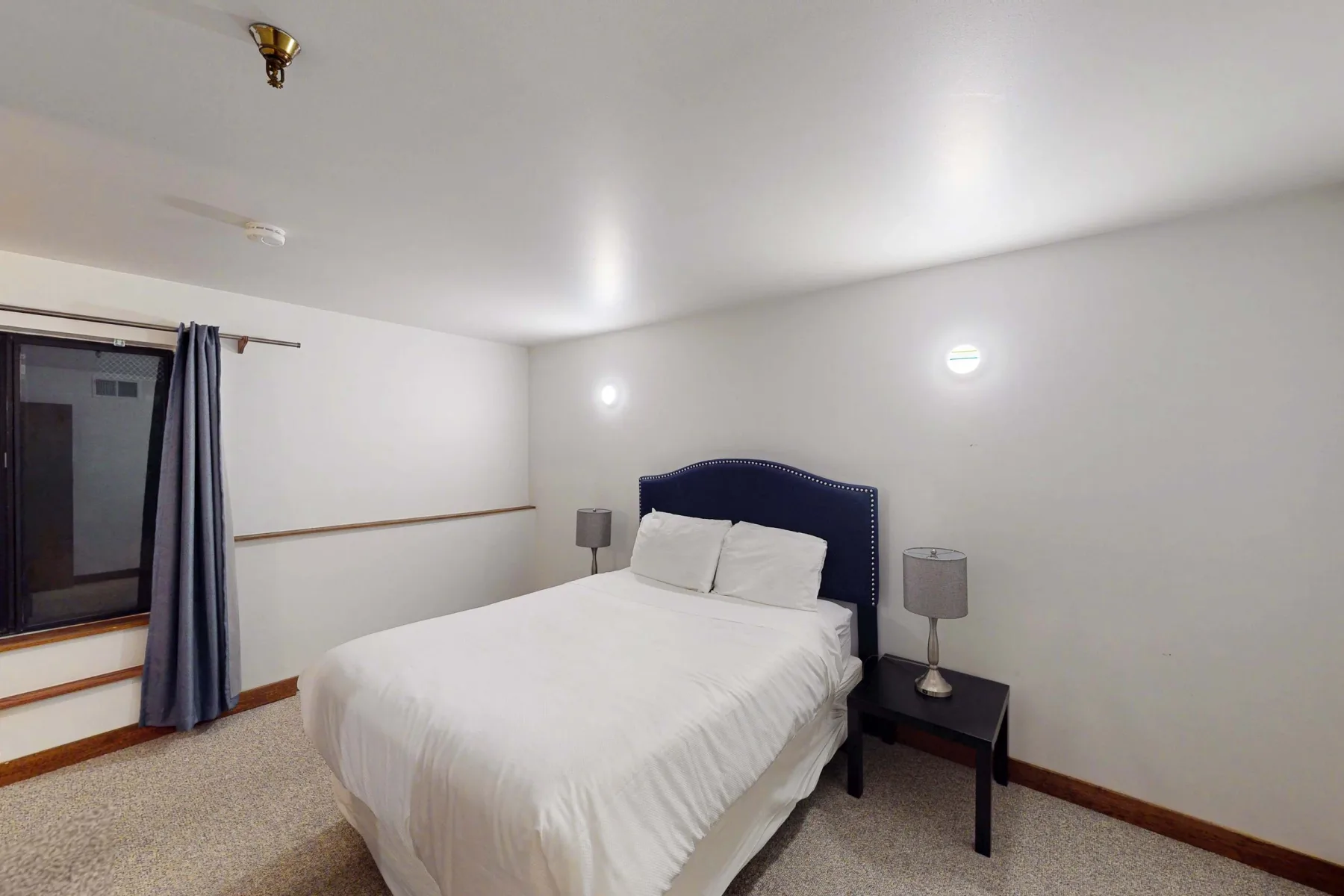 Un dormitorio con una cama, mesitas de noche y una ventana con cortinas.