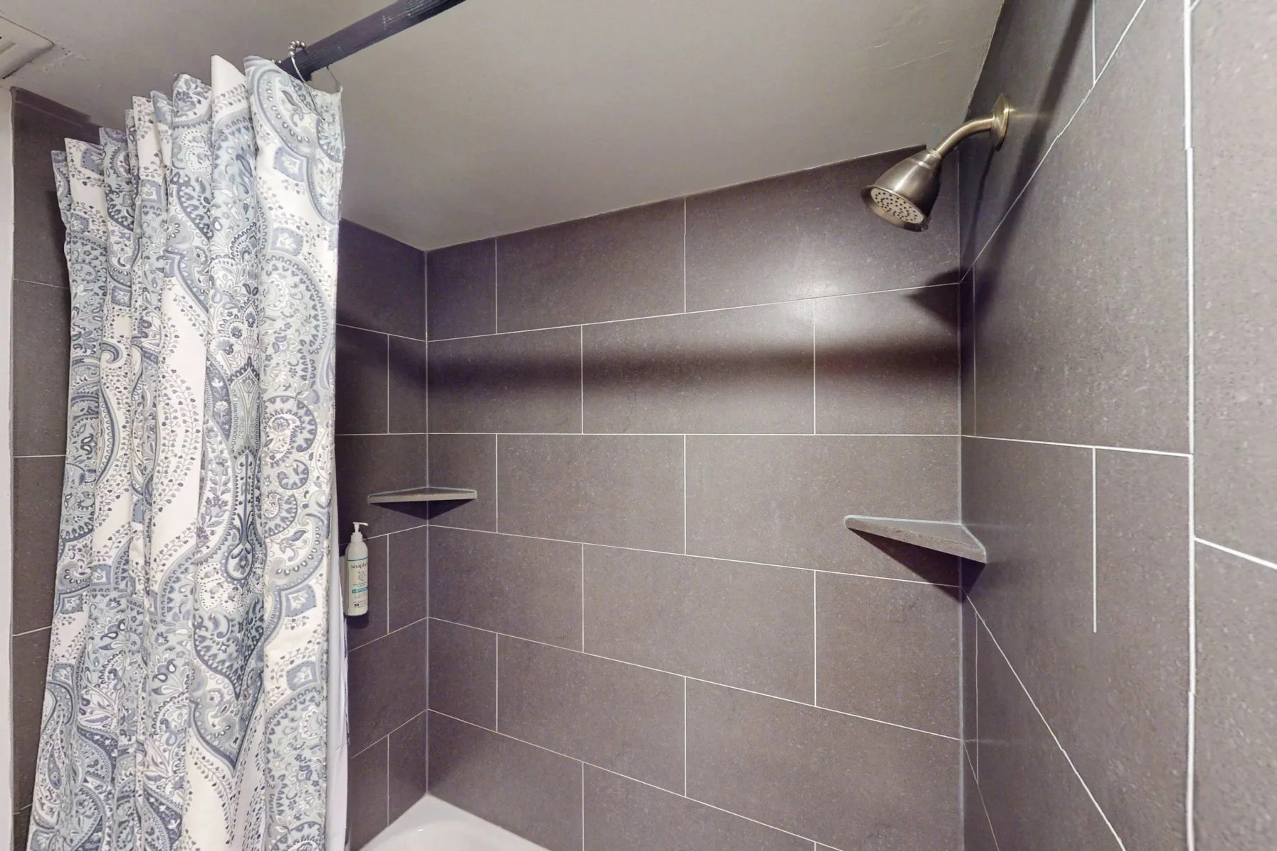 Una ducha de baño con azulejos, cortina estampada y cabezal montado en la pared.