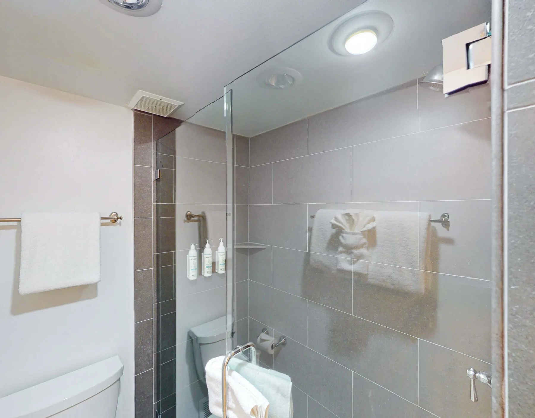 Un baño con azulejos, una ducha de vidrio, toallas y un inodoro.
