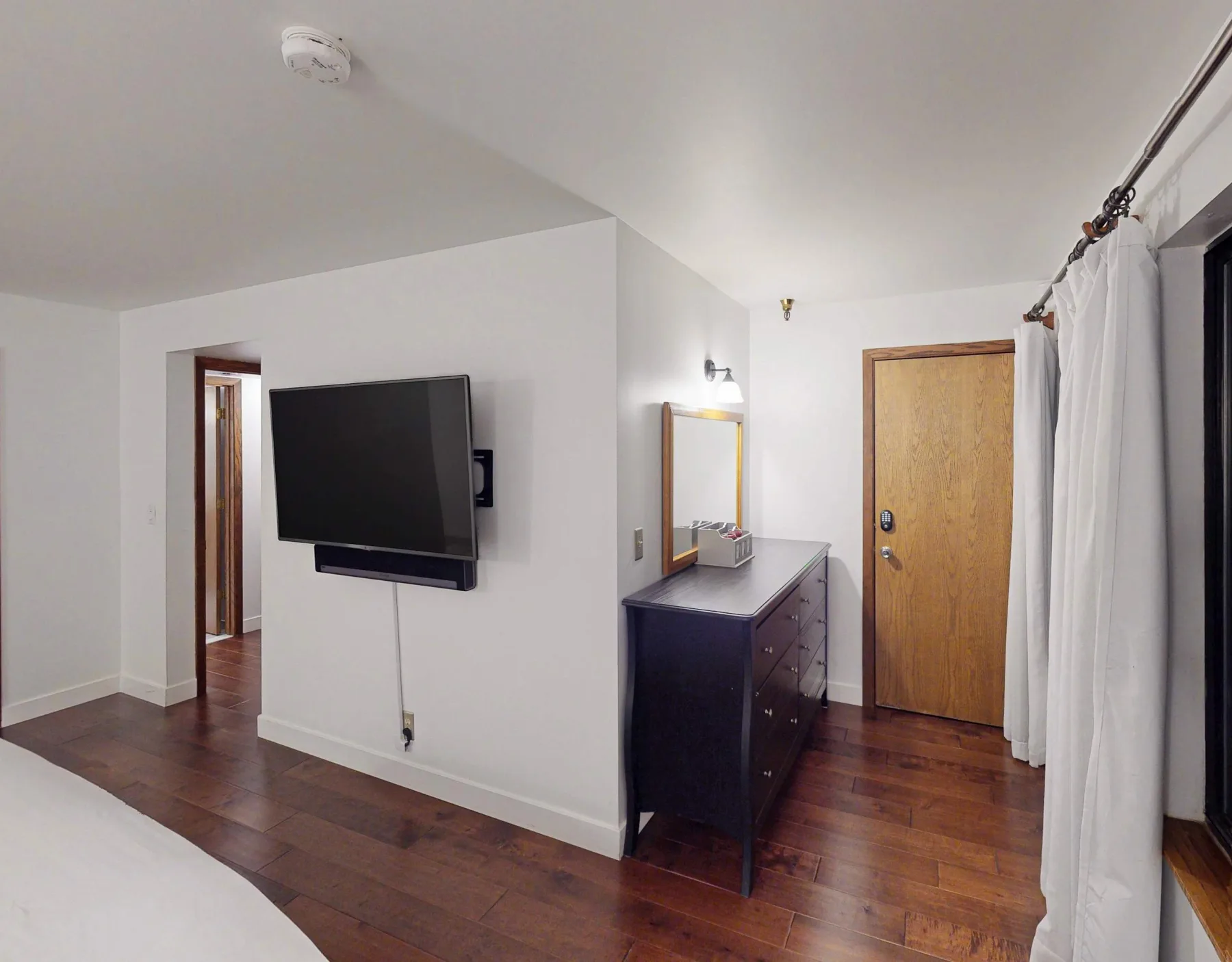 Un dormitorio con televisor en la pared, cómoda y ventana con cortinas.