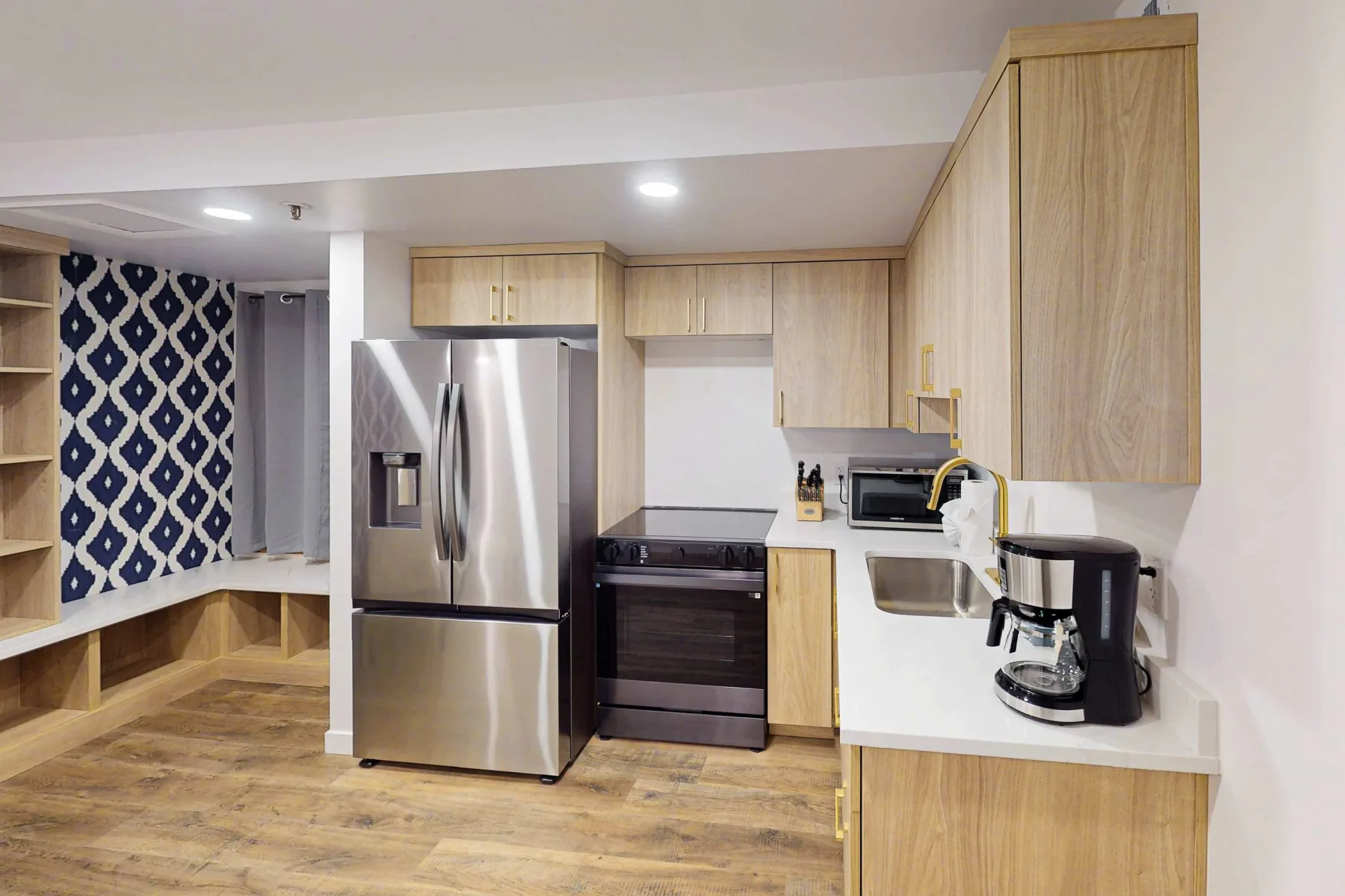 Una cocina compacta con gabinetes de madera clara, electrodomésticos de acero inoxidable y una encimera blanca.