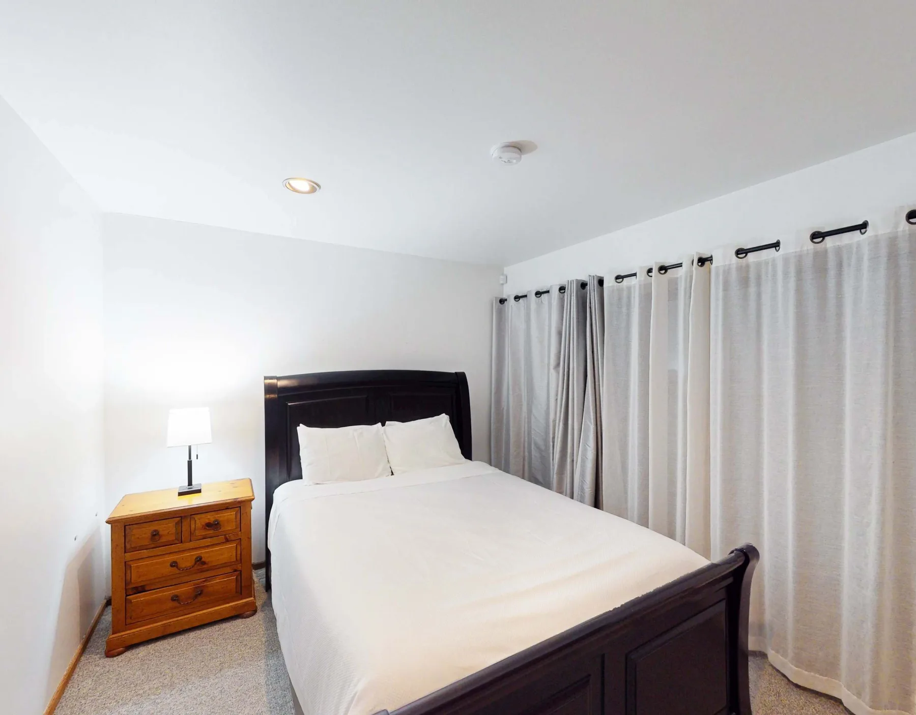 Un dormitorio con una cama, una mesita de noche y cortinas.