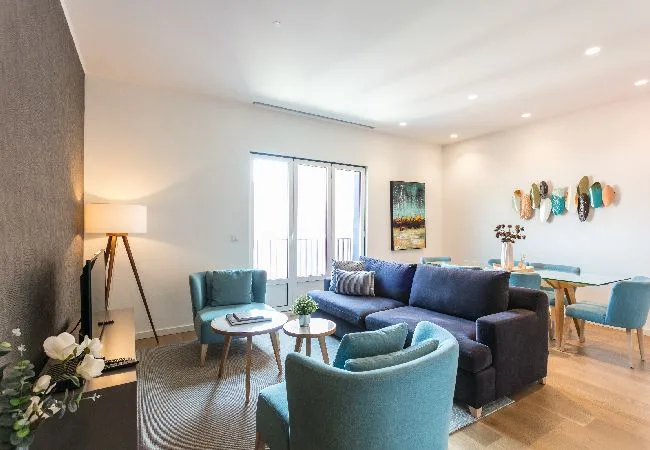 A bright living room with blue seating, a coffee table, and a dining area.