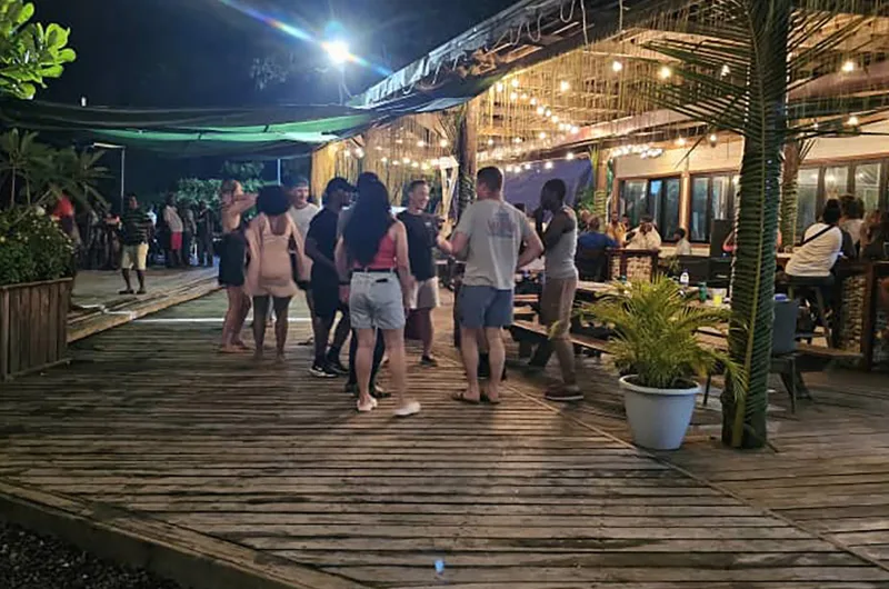 Espacio representativo del hotel: Una animada zona de comedor al aire libre de noche, con gente reunida en una terraza de madera.