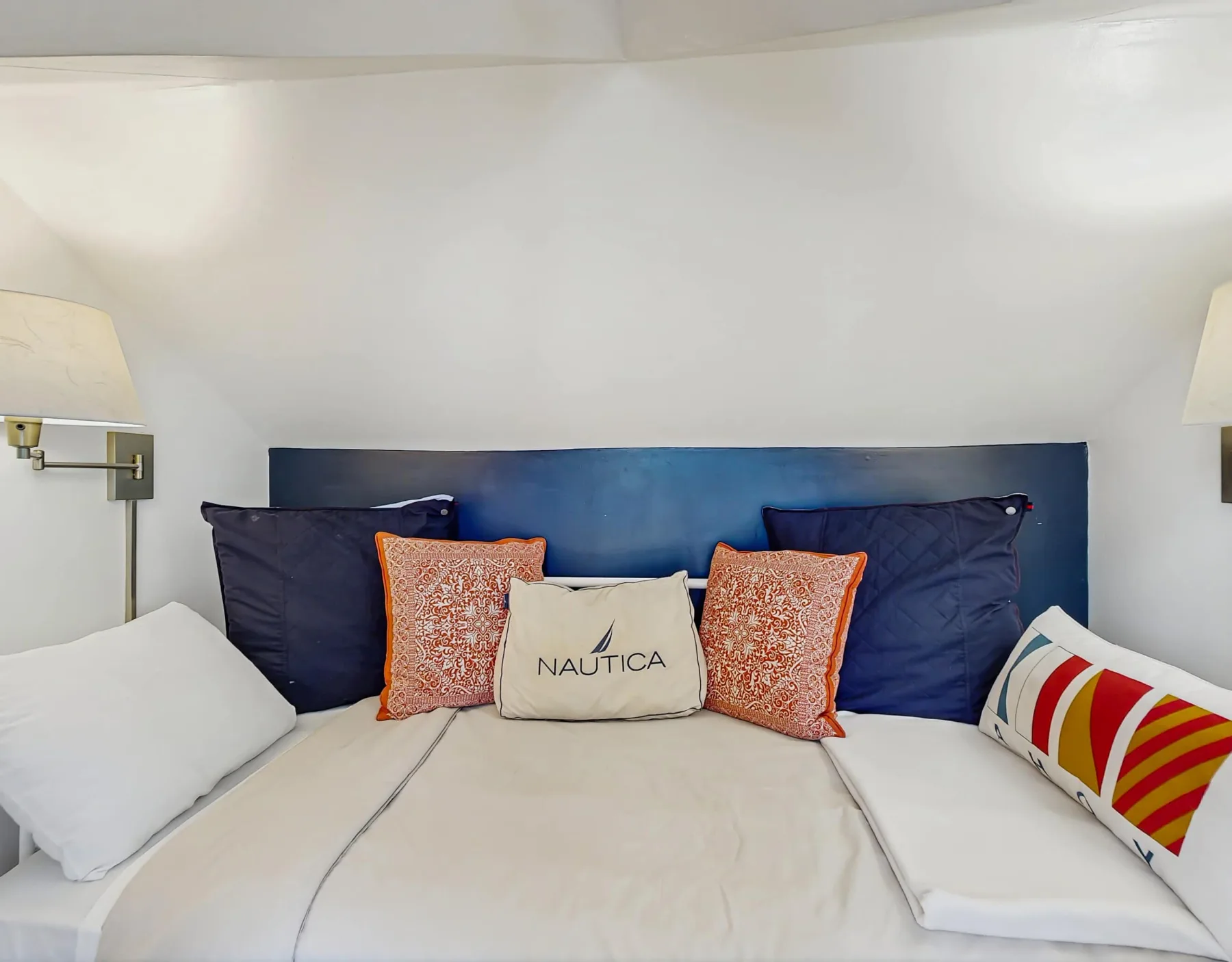 Una cama con ropa de cama blanca y cojines coloridos está junto a un cabecero azul oscuro.