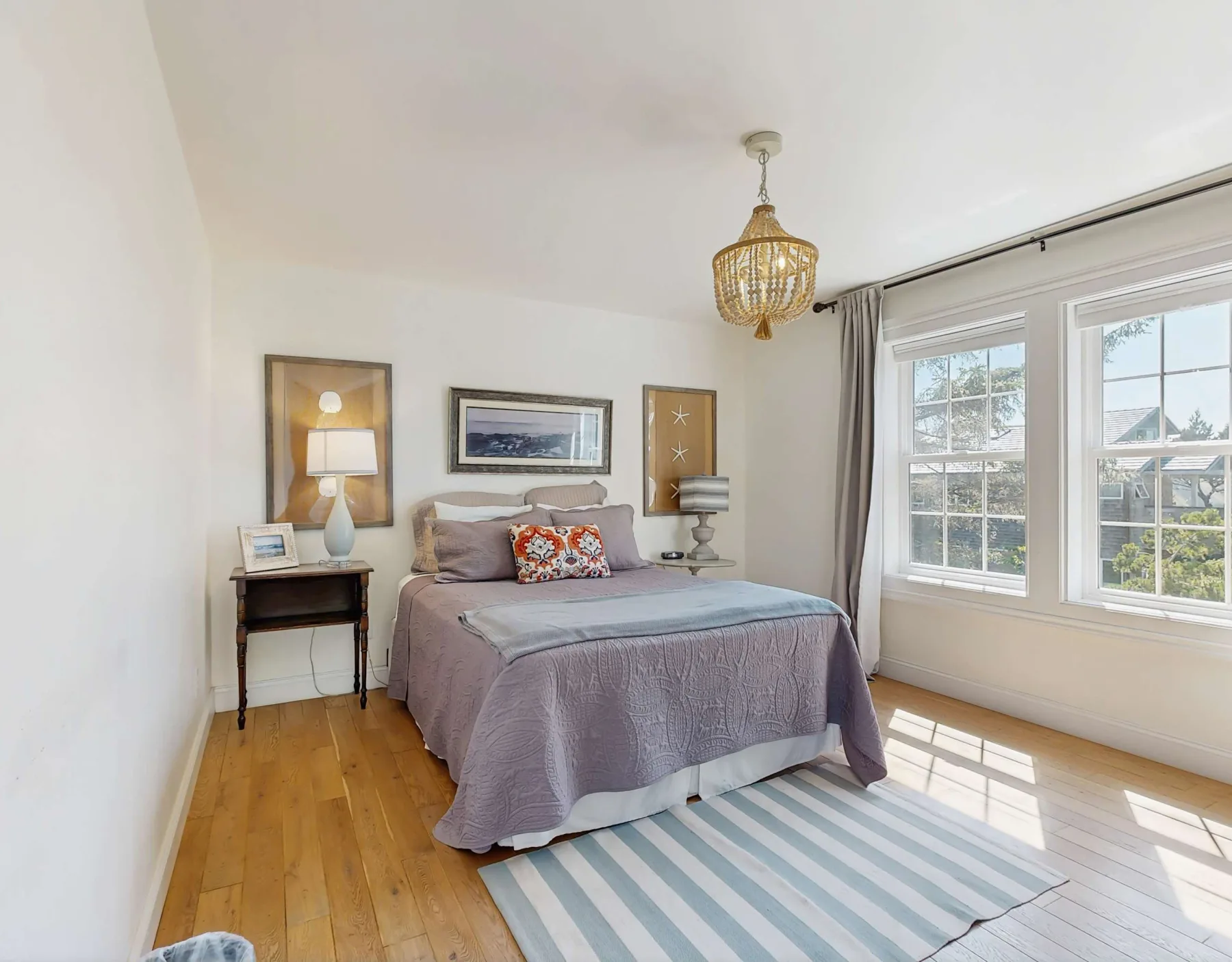 Un dormitorio luminoso con una cama, mesitas de noche y grandes ventanas.
