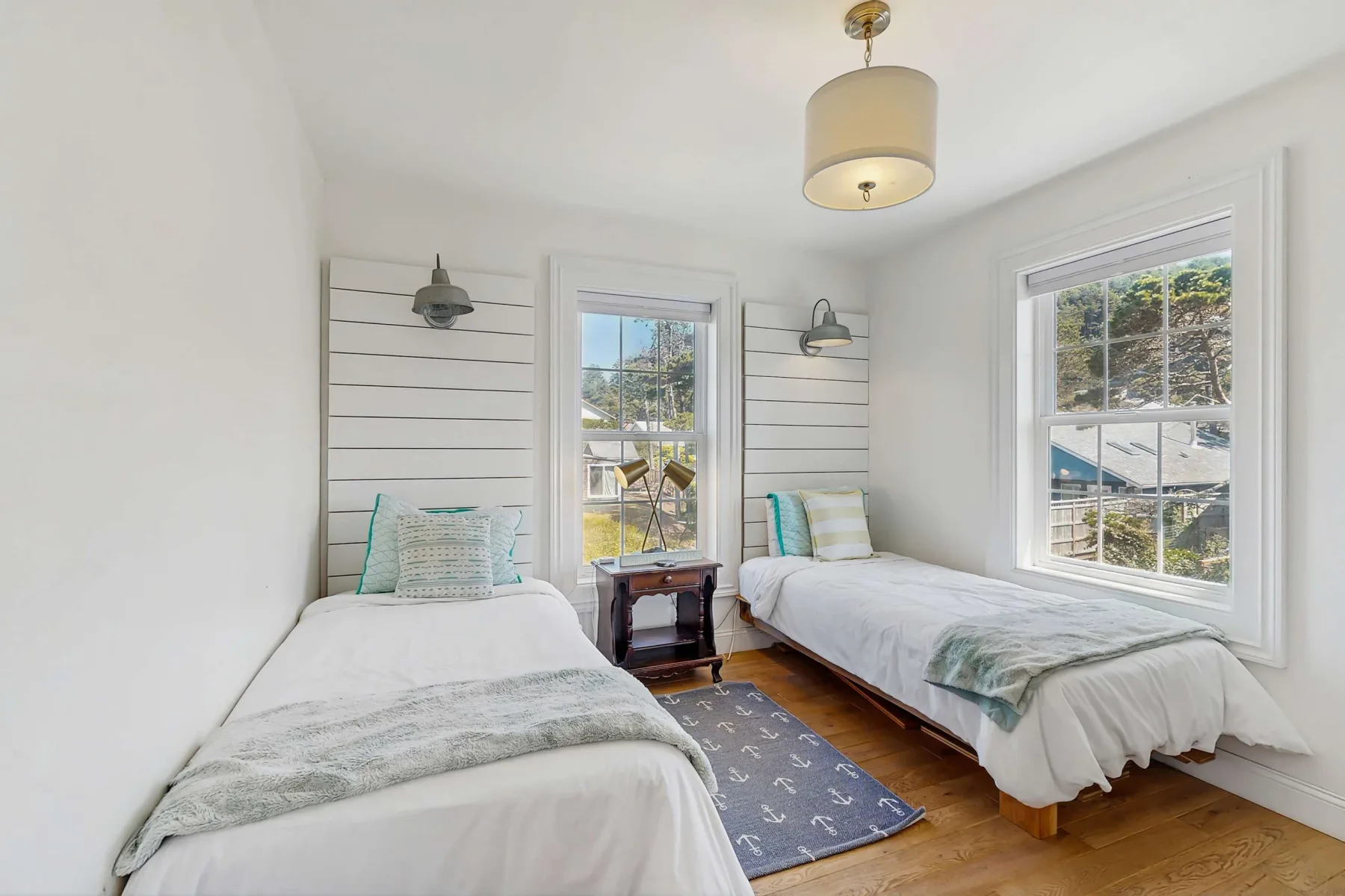 Un dormitorio luminoso con dos camas individuales y ventanas con vistas a la vegetación.