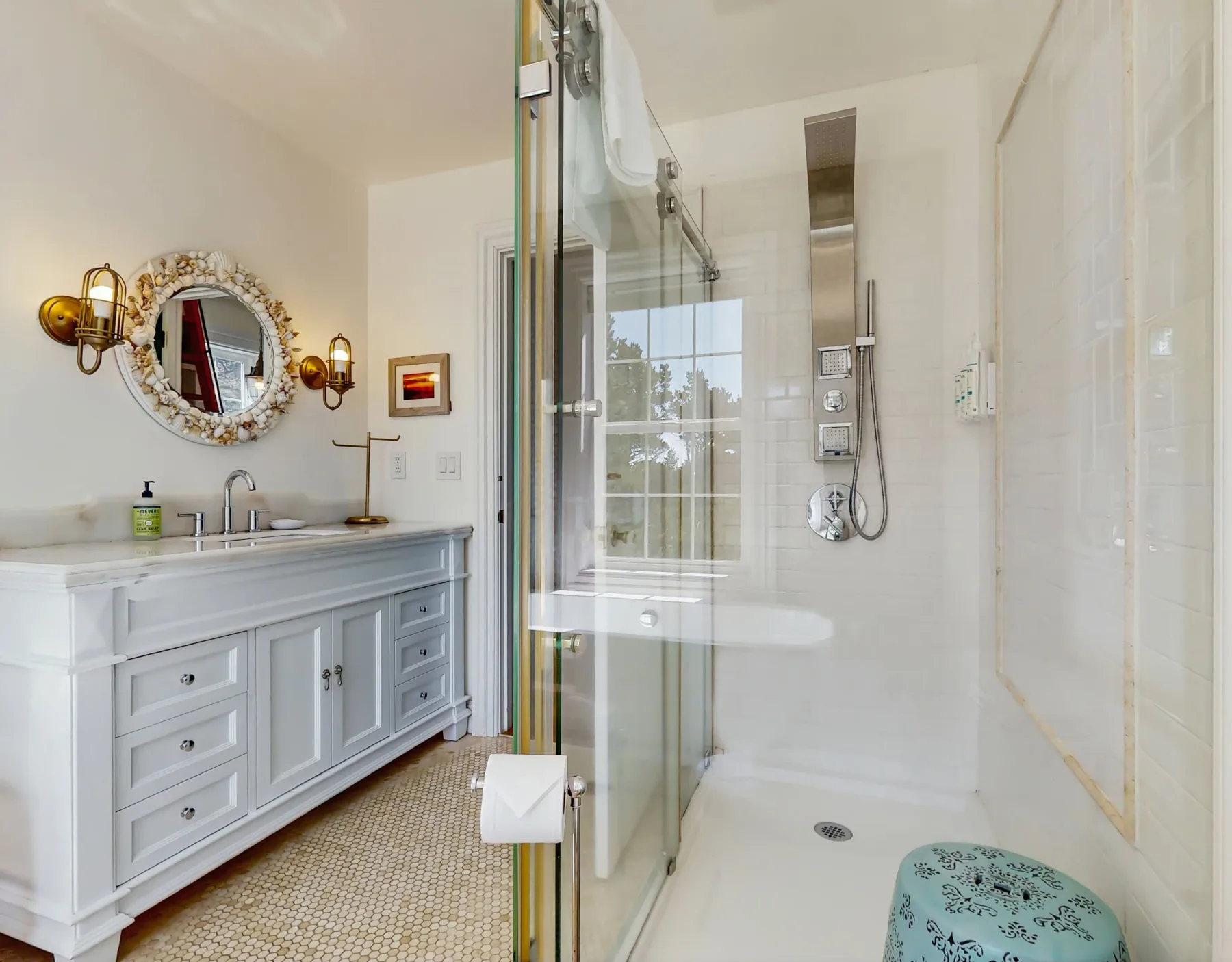 Un baño luminoso con tocador, espejo redondo y ducha de cristal.