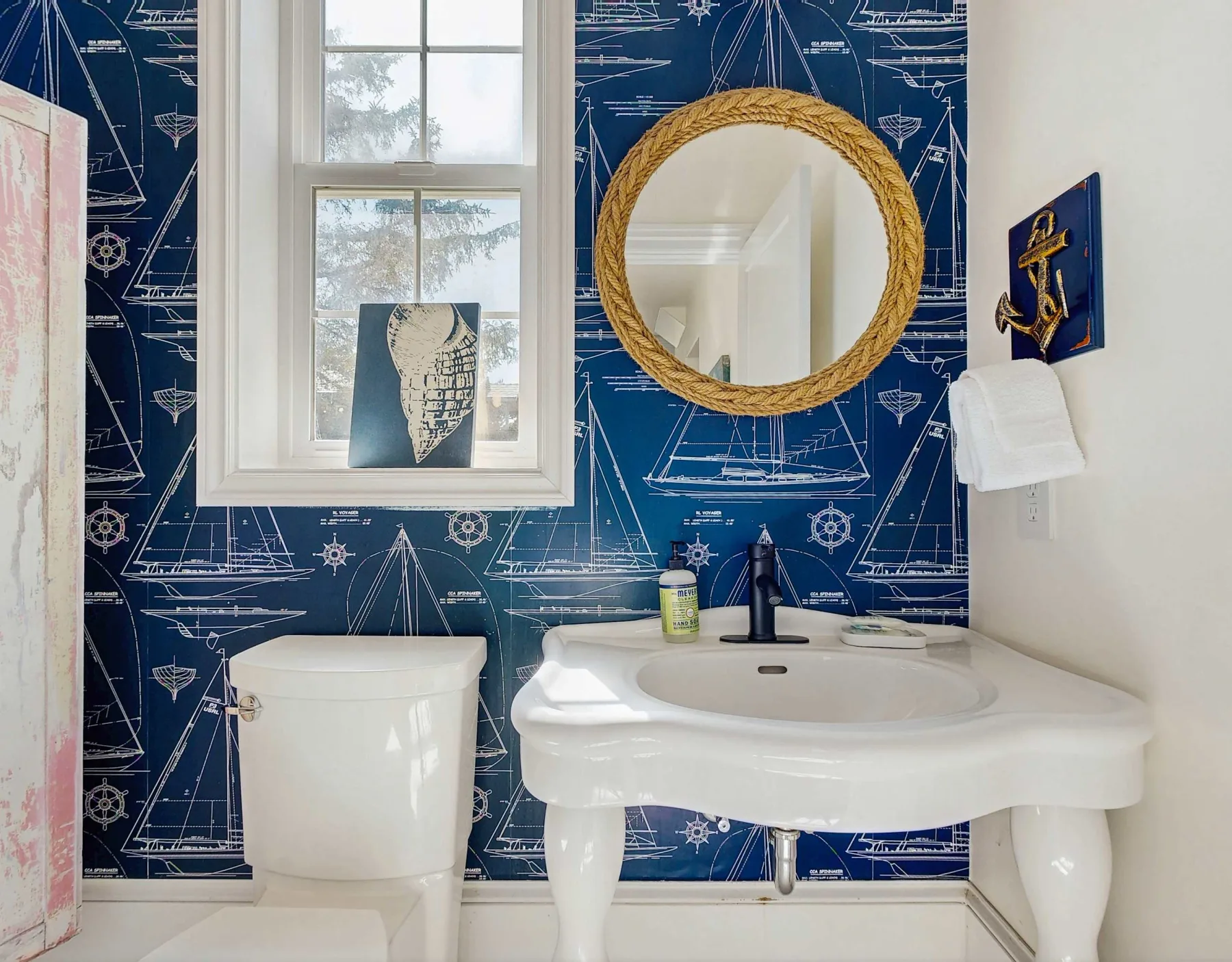 Un baño con lavabo e inodoro blancos frente a paredes azul oscuro estampadas.