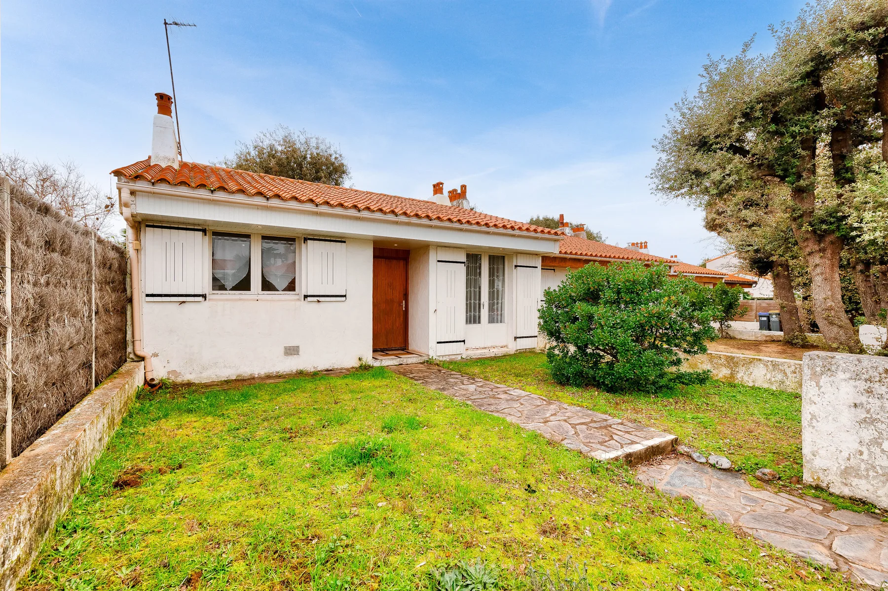 A single-story house with a tiled roof faces a grassy yard and stone walkway.