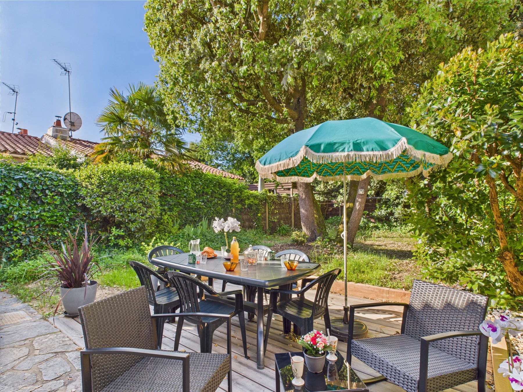 An outdoor patio has a dining table and seating beneath a green umbrella.