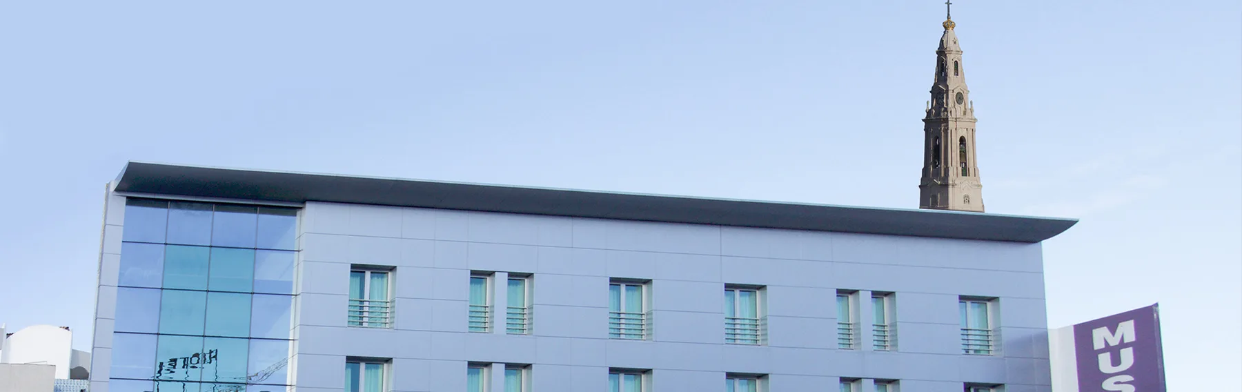 Espacio representativo del hotel: Un edificio moderno con una alta aguja de piedra que sobresale detrás del techo.