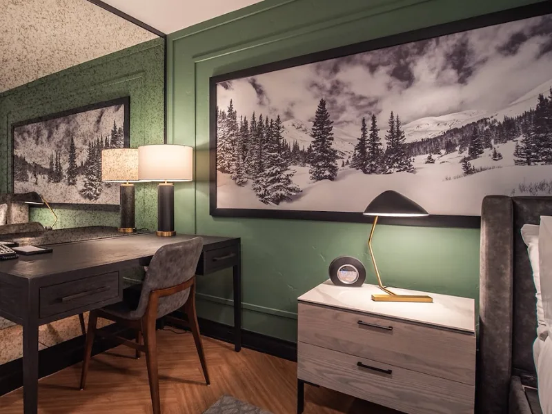 Representative hotel space: A bedroom workspace with a desk, bedside dresser, and snowy landscape artwork.
