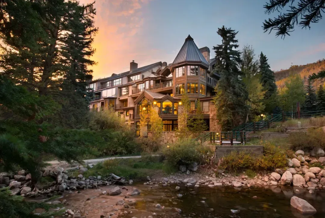 Representative hotel space: A lodge stands beside a rocky stream beneath a colorful sunset sky.