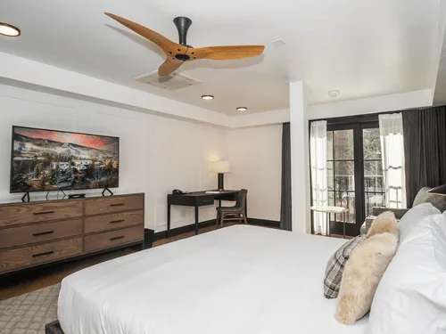 Representative hotel space: A bedroom with a bed, dresser, and desk beside tall windows.