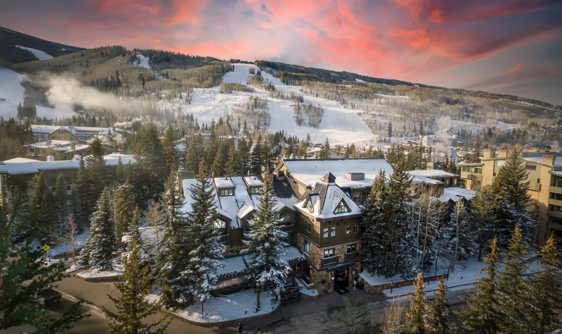 Representative hotel space: Snow-covered resort buildings sit among trees below a mountain ski slope at sunset.