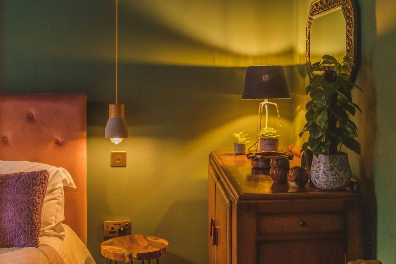 A warmly lit bedroom with a bed, bedside table, and dresser.