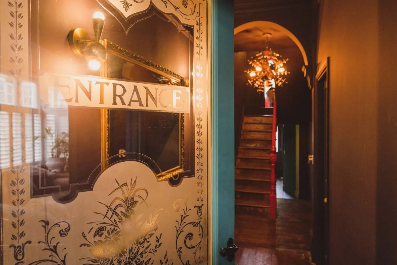 An ornate entrance panel overlooks a dim hallway with a staircase and hanging light.