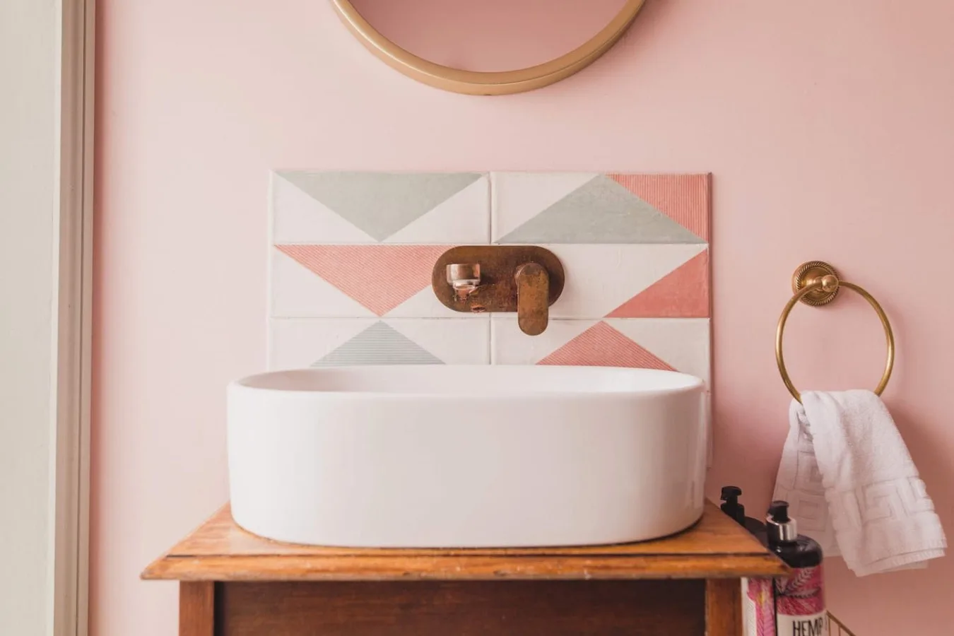 A bathroom vanity with a white vessel sink against a pink wall.
