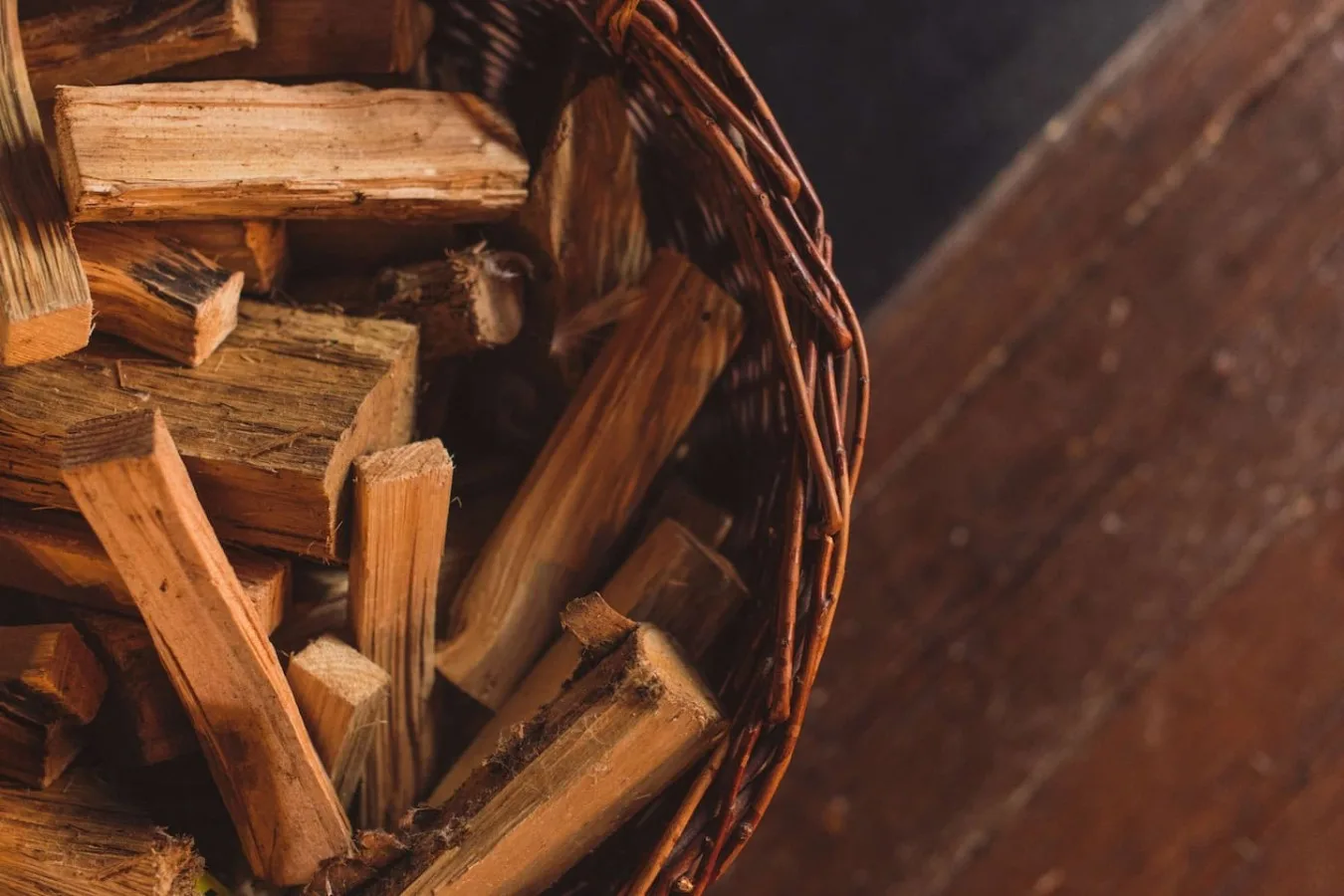 A woven basket filled with split firewood rests on a wooden surface.