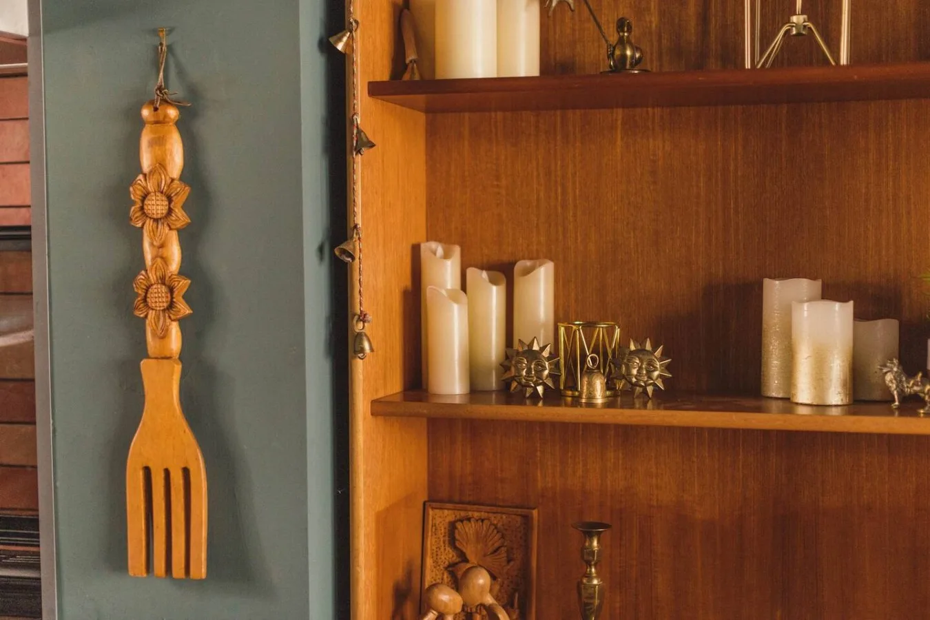 A wooden display shelf holds candles and small decorative objects beside a carved wooden ornament.
