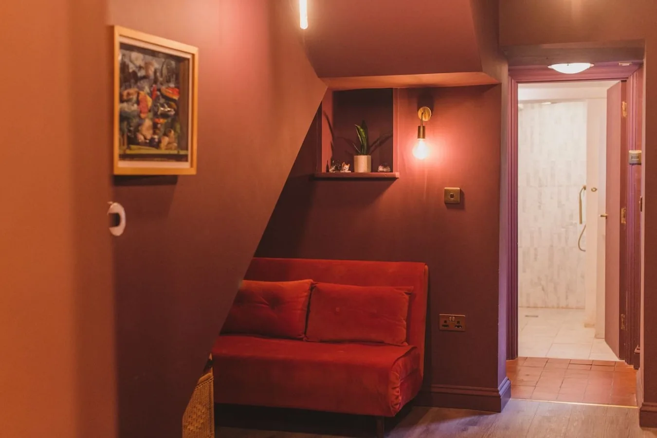 A warmly lit hallway with red seating and an open doorway to a tiled room.