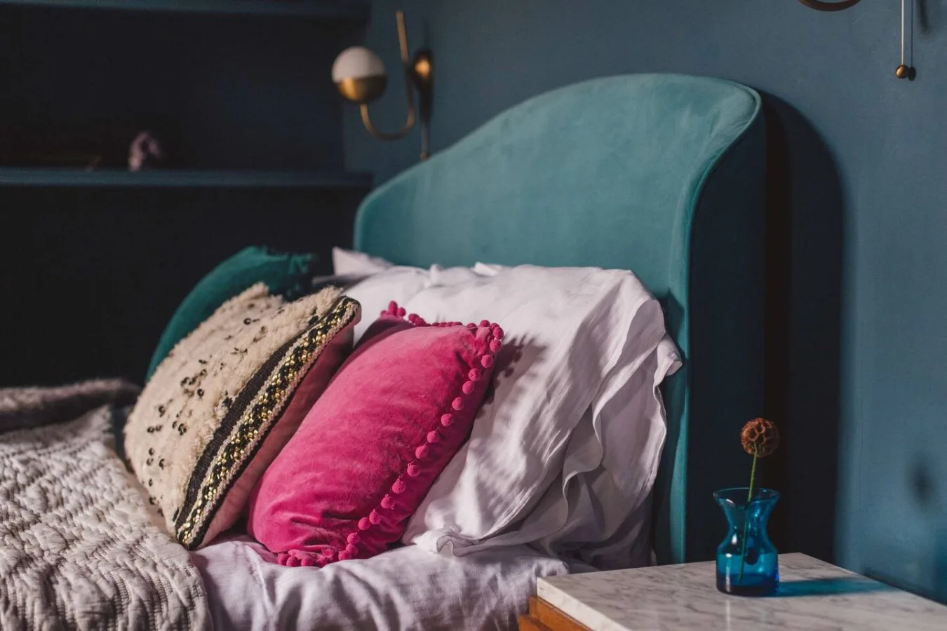 A bedroom with colorful pillows arranged against a curved teal headboard.