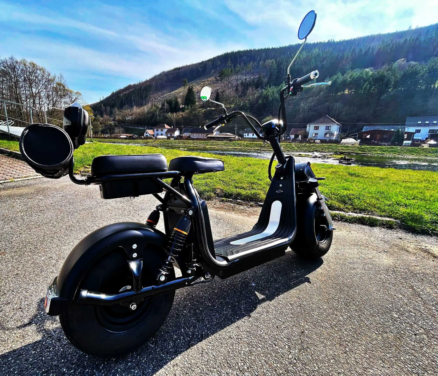 Espacio representativo del hotel: Un scooter negro está junto a un campo de hierba, con colinas boscosas al fondo.
