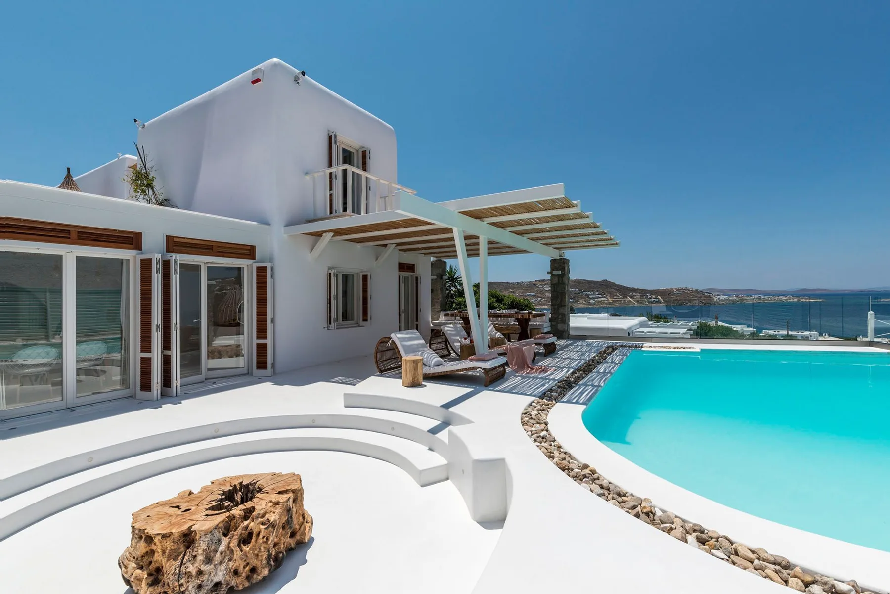 A white villa opens onto a curved swimming pool beside a pergola.