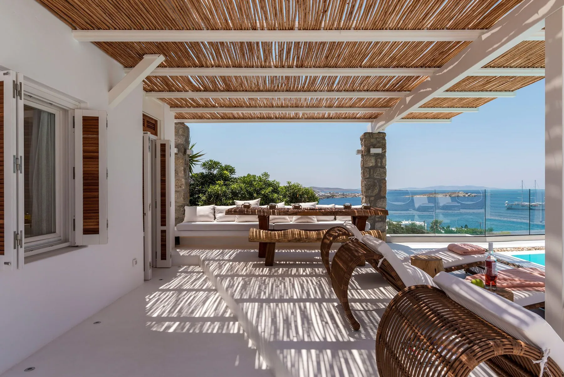 A covered outdoor seating area overlooks a pool and the sea.