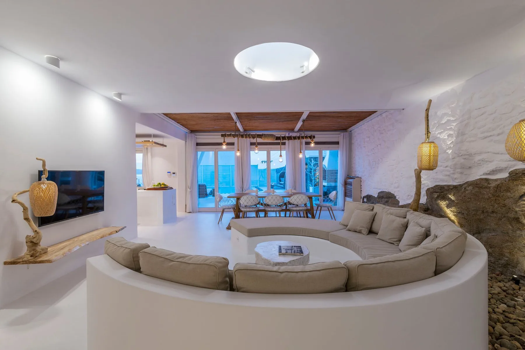A curved living room seating area faces a wall-mounted television, with glass doors beyond.