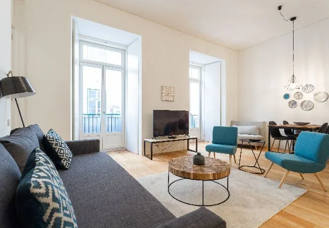 Una sala luminosa con asientos, un televisor y ventanas altas.