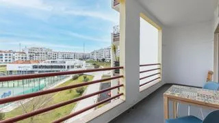 Un balcón cubierto da a edificios cercanos y tiene una mesa pequeña y asientos.
