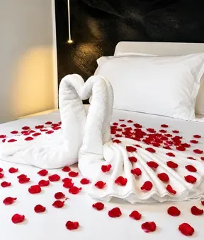 Espacio representativo del hotel: Una cama de hotel está decorada con toallas blancas y pétalos rojos esparcidos.
