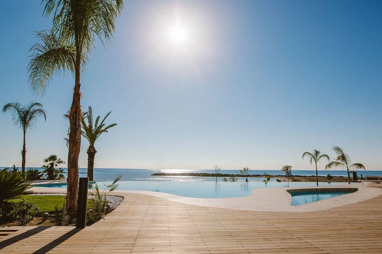 Espacio representativo del hotel: Una piscina al aire libre y una terraza de madera dan al mar bajo un cielo luminoso.
