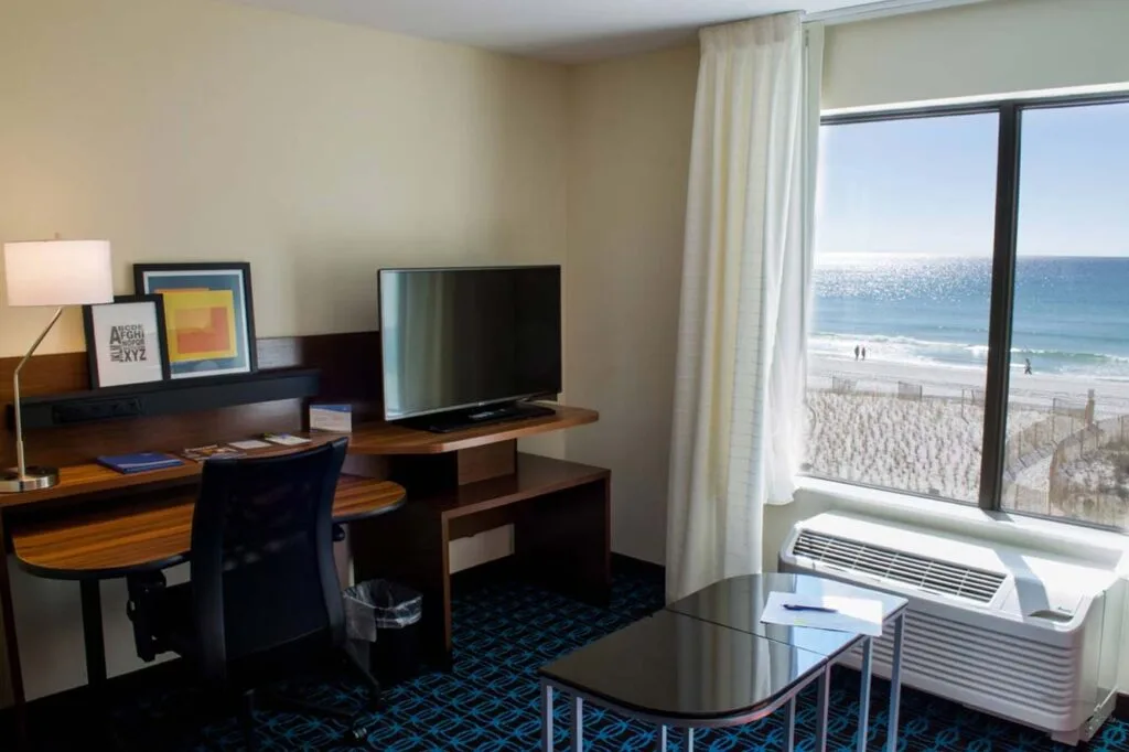 Espacio representativo del hotel: Una habitación de hotel tiene un escritorio y un televisor junto a una ventana con vista a la playa.