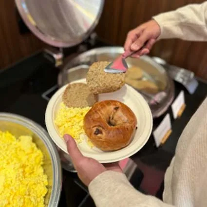 Espacio representativo del hotel: Una persona se sirve el desayuno en un bufé con huevos revueltos y un bollo.